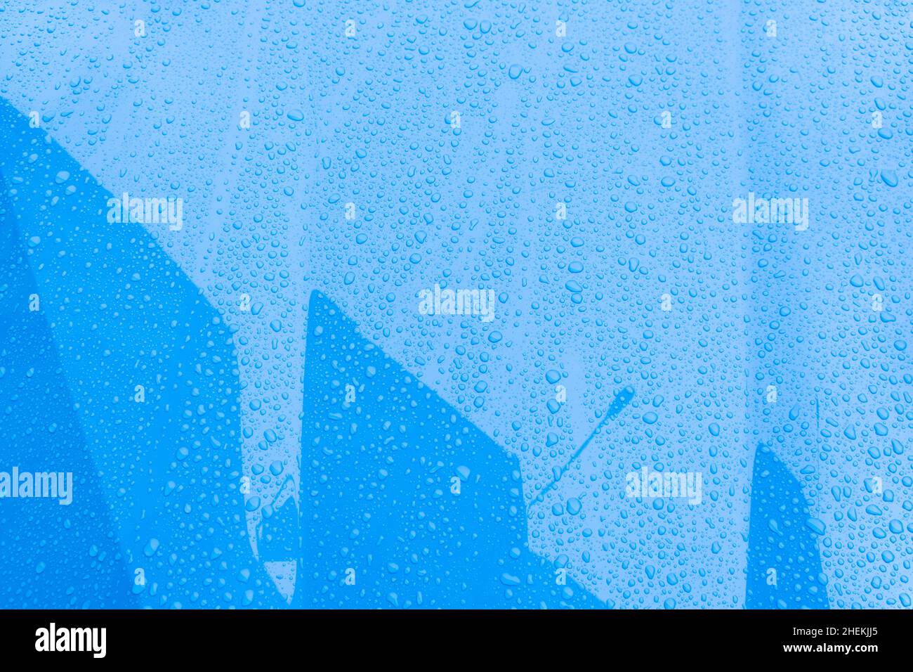 Superficie blu dell'auto con gocce d'acqua. Primo piano gocce d'acqua con riflessione edificio in autunno piovoso giorni. Pioggia bagnato tempo sfondo Foto Stock