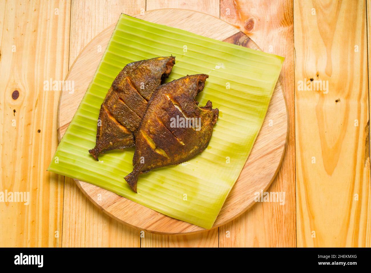 Frittura di pesce Pomfret disposta su una foglia di banana posta su base di legno. Foto Stock