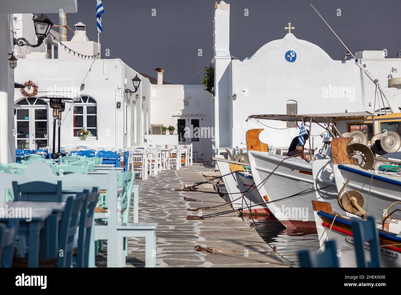 Grecia, Paros isola Naousa porto vecchio. Barca da pesca ormeggiata al molo del porto, tavolo da caffè e sedie all'aperto sul mare. Foto Stock