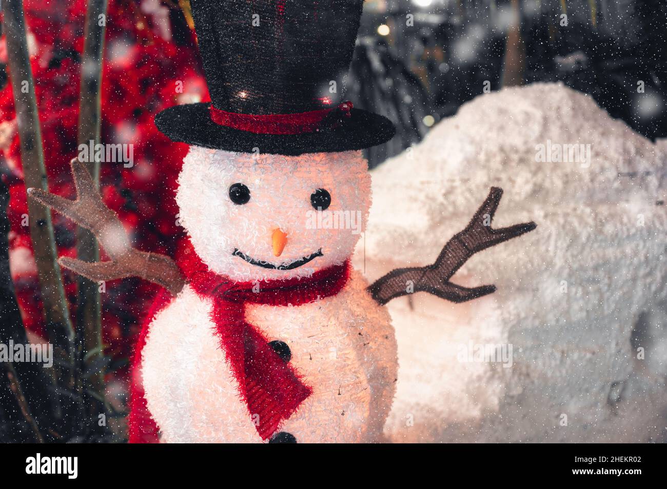 Carino pupazzo di neve con cappello e sciarpa in nevicata decorare in cortile sul festival di Natale Foto Stock