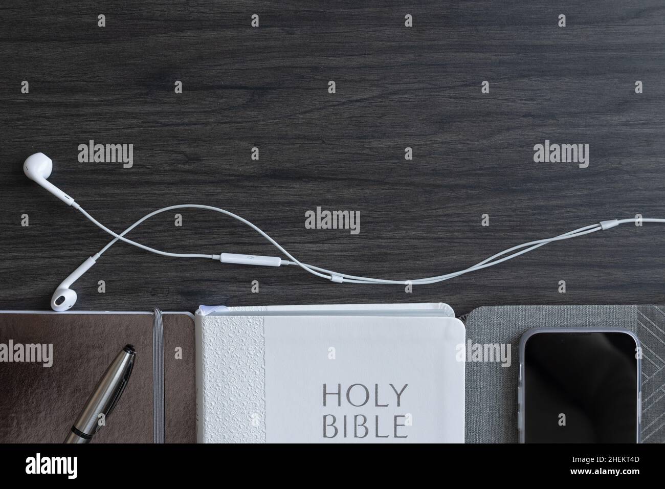 Bordo della bibbia bianca, diari grigi, telefono cellulare e auricolari su sfondo di legno scuro con spazio copia Foto Stock