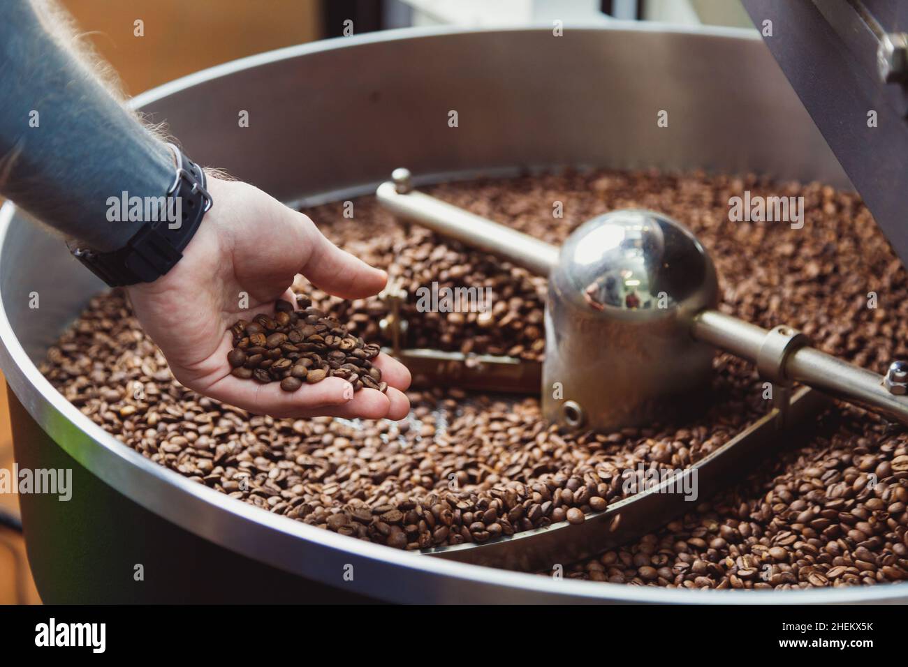 Man controllare i chicchi di caffè torrefatti sulla piastra di raffreddamento dell'tostatore industriale. Torrefazione di fagioli industriali. Vista dall'alto Foto Stock