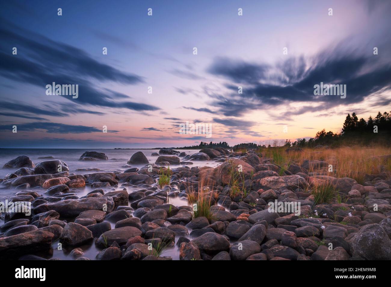 Lunga esposizione di un magnifico tramonto morbido e colorato vicino alla pietra del mare. Bel movimento nube con pietre di mare. Foto Stock