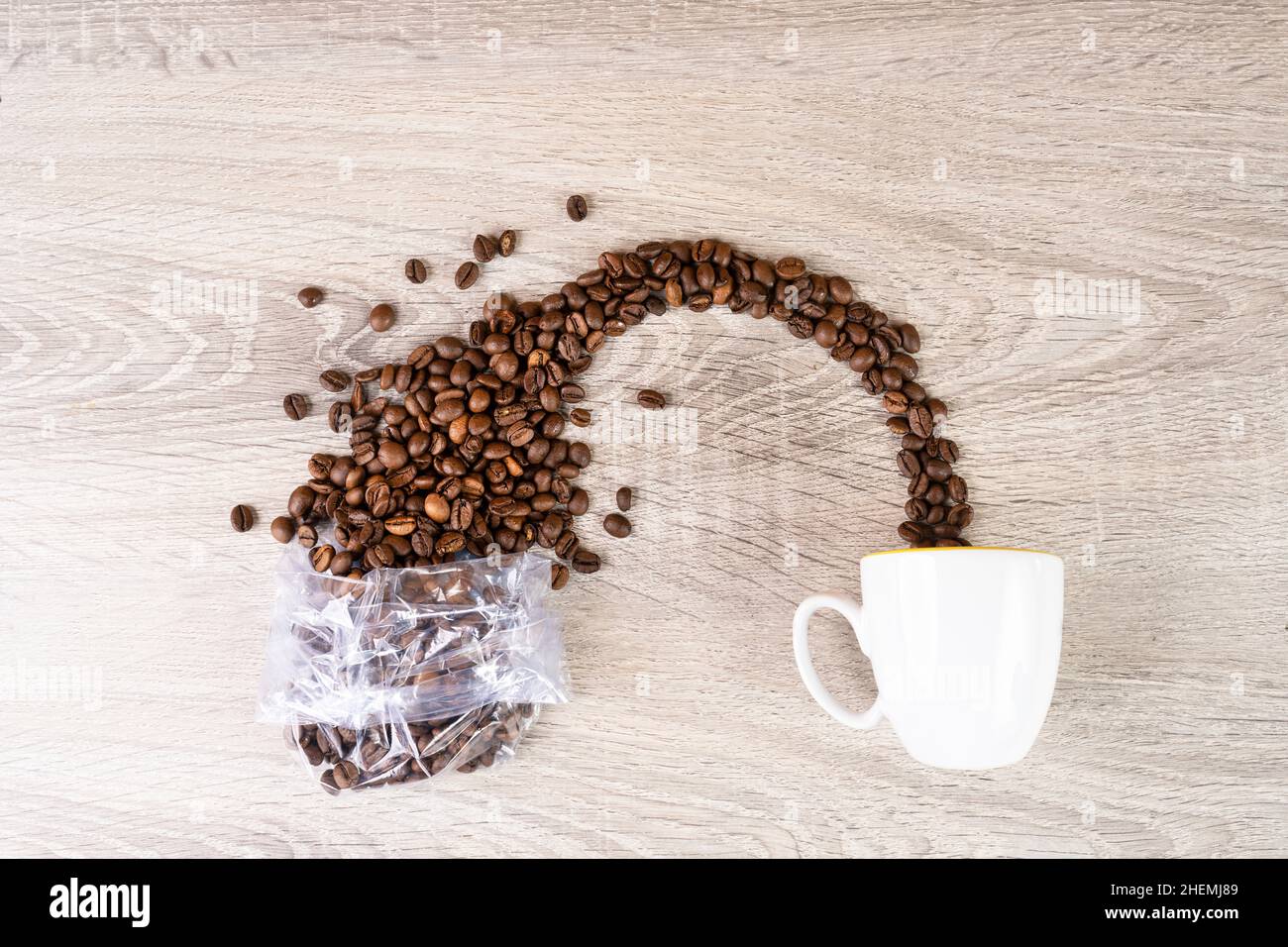 i chicchi di caffè fuoriescono da un sacchetto di plastica trasparente in una tazza Foto Stock