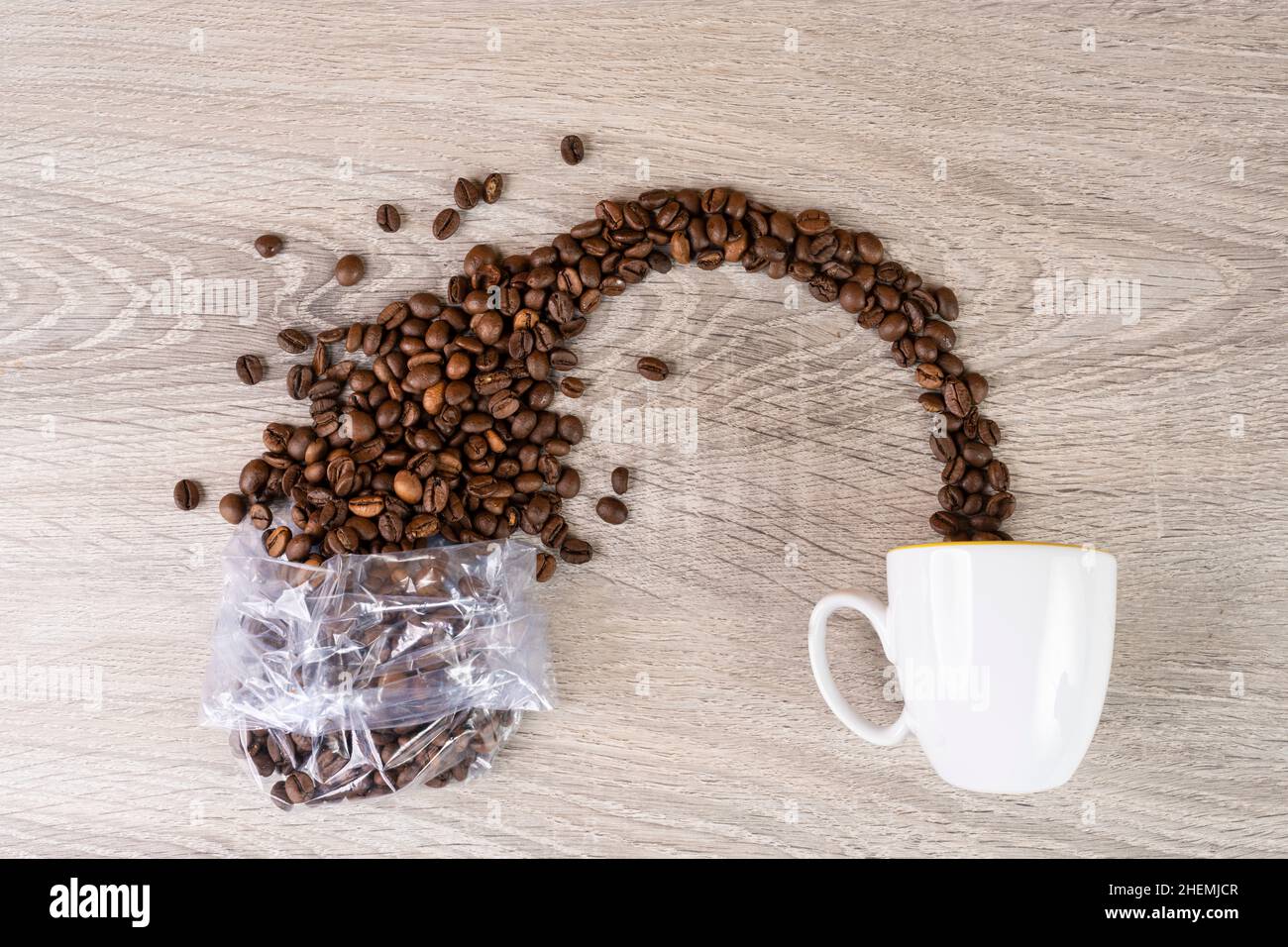 i chicchi di caffè fuoriescono da un sacchetto di plastica trasparente in una tazza Foto Stock