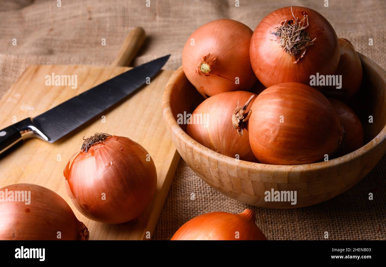 Cipolle rosse e bianche su un tagliere di legno e coltello su un rustico tavolo di legno in cucina, vista dall'alto. Foto di alta qualità Foto Stock