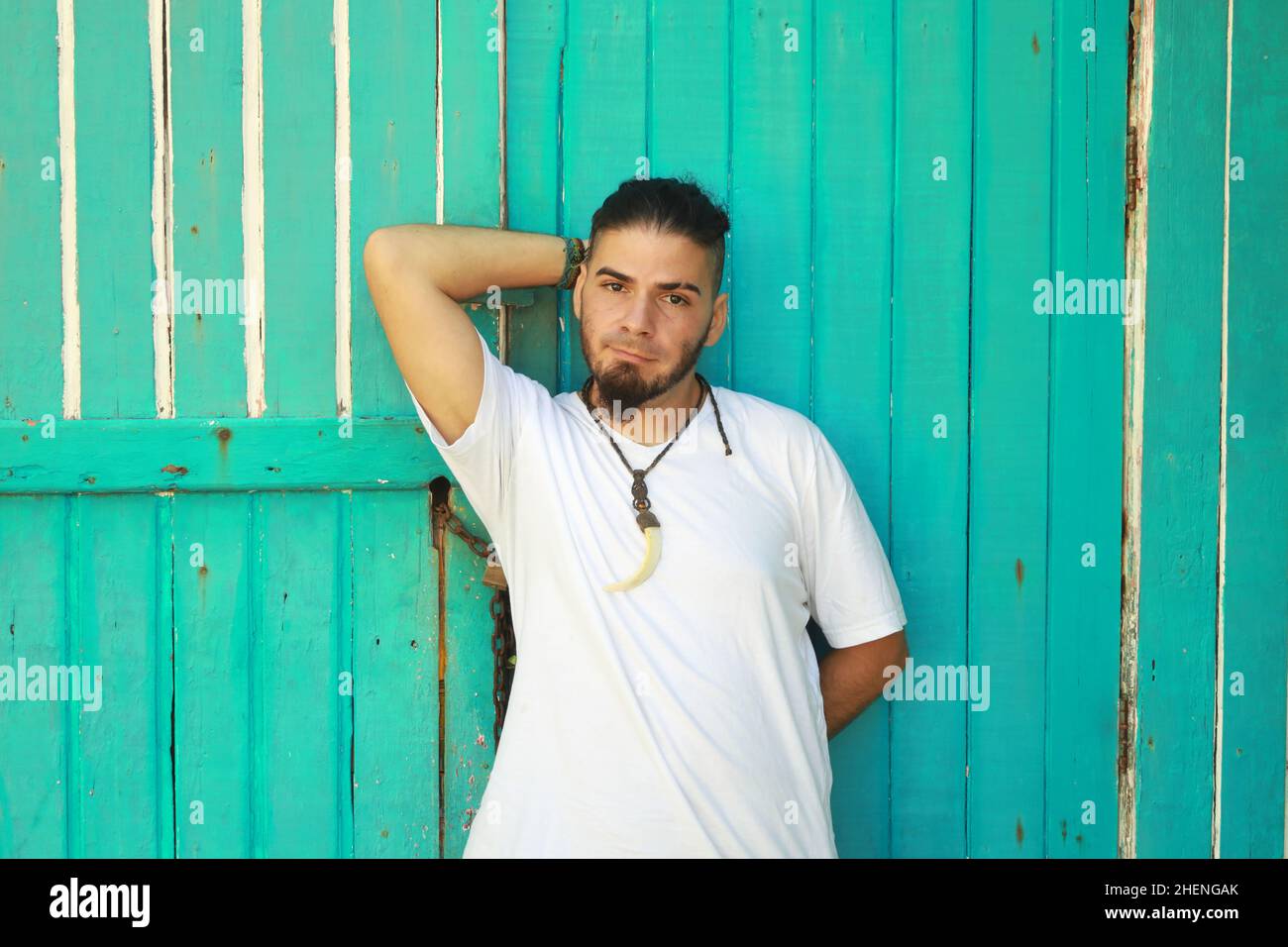 Giovane uomo in camicia bianca e la mano dietro la testa accanto ad un muro di legno verde. Foto Stock