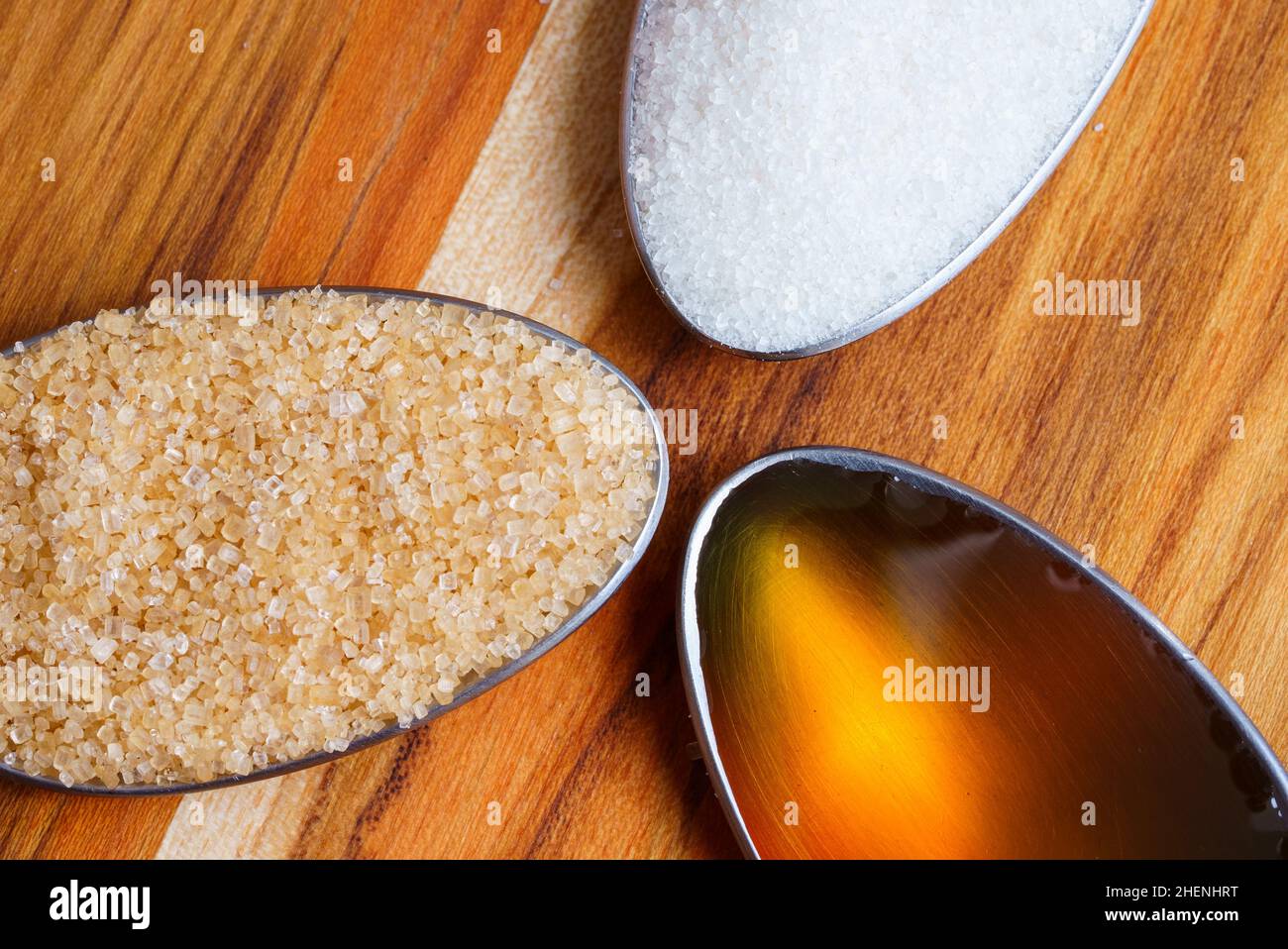Primo piano vista dall'alto verso il basso di cucchiai con zucchero di canna, miele crudo e zucchero bianco su tavola di legno Foto Stock