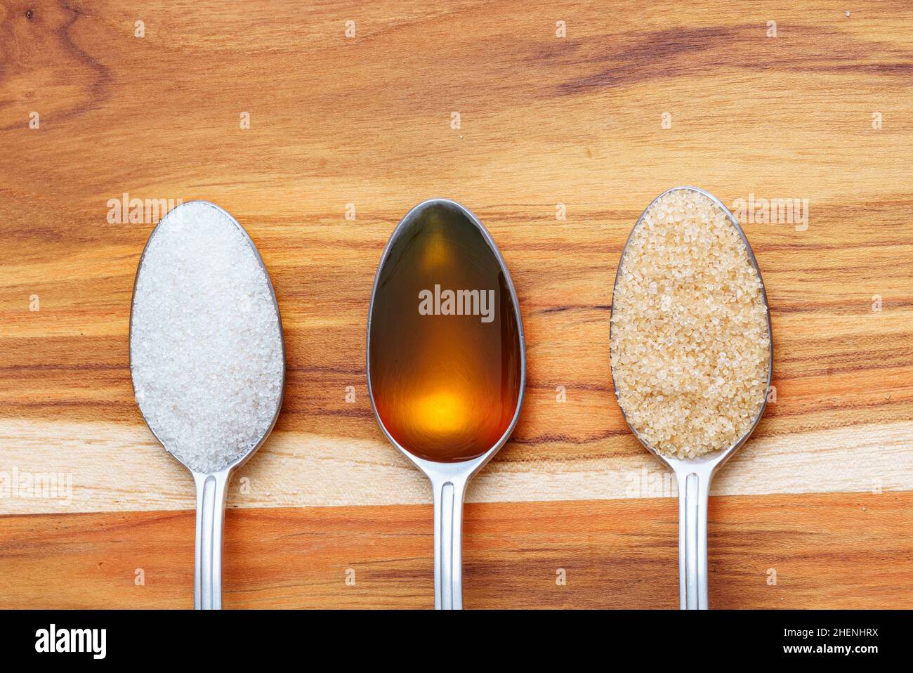 Cucchiai con zucchero bianco, miele crudo e zucchero di canna su tavola di legno Foto Stock
