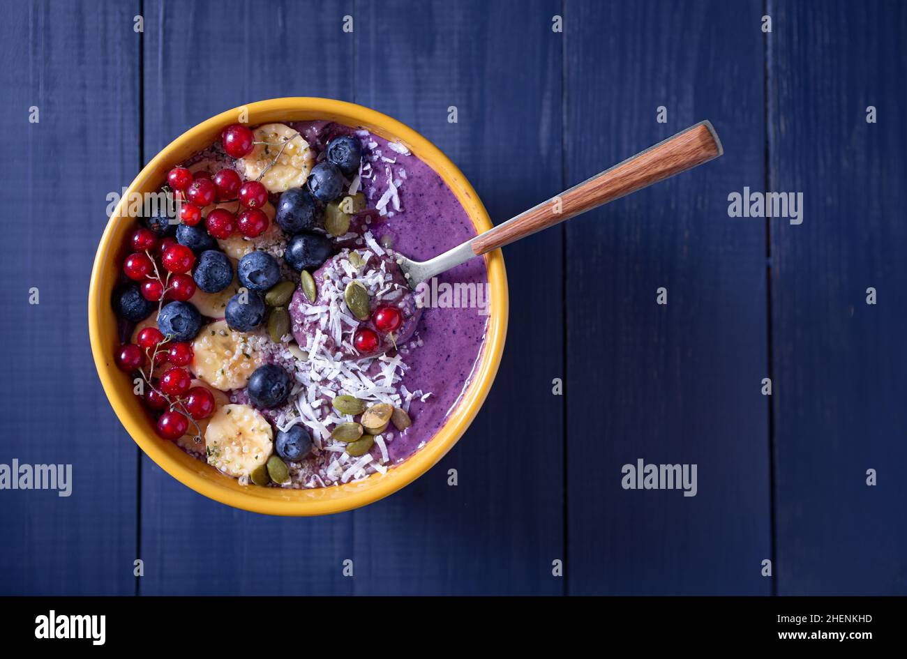 Vista dall'alto di una salubre ciotola di frullato di frutti di bosco crudi su una superficie di legno blu con spazio per la copia Foto Stock