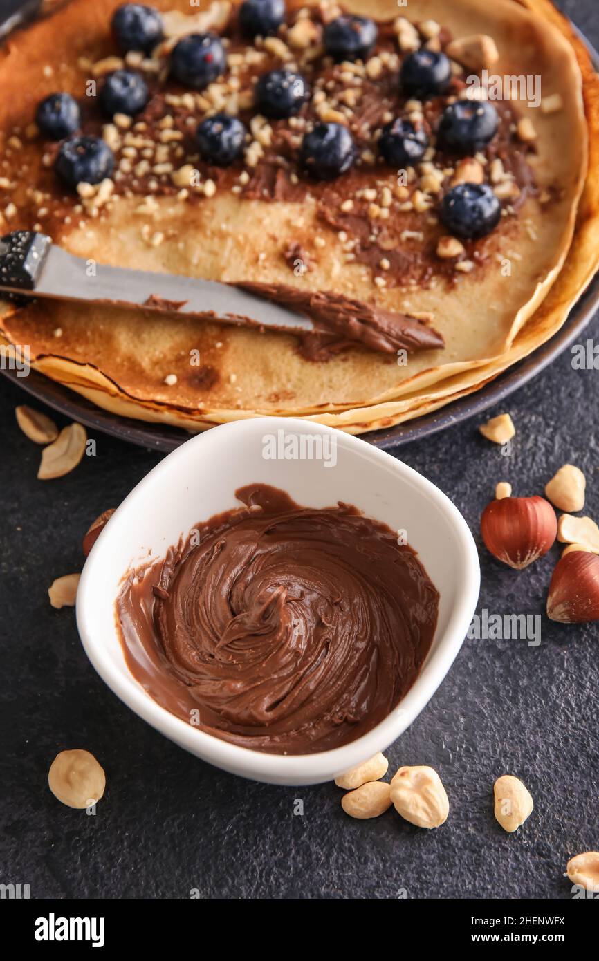 Ciotola con gustosa pasta di cioccolato, noci e crepes su sfondo nero Foto Stock