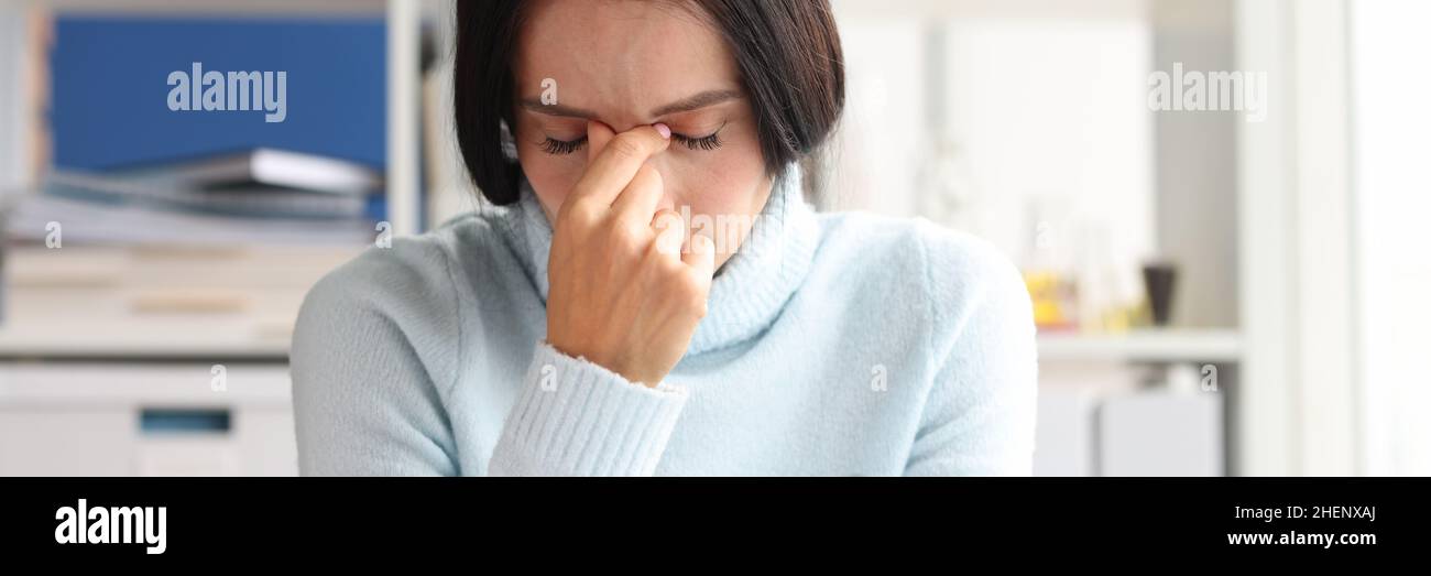 La donna depressa dolorosa si siede con gli occhi chiusi sul posto di lavoro Foto Stock