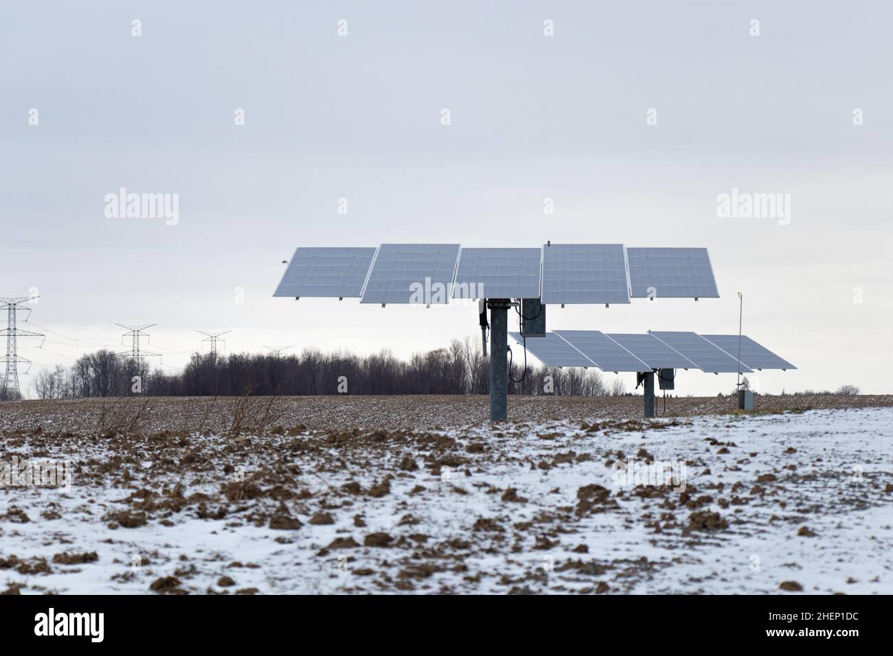 Un paio di inseguitori solari, che orientano i pannelli solari verso il sole, è visto in una zona rurale in un pomeriggio nevoso. Foto Stock