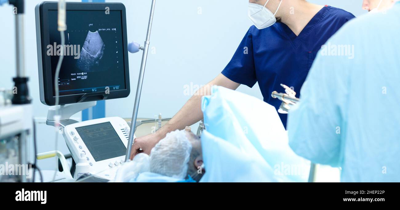 Controllo a ultrasuoni degli organi interni del paziente durante l'intervento chirurgico. I medici guardano un monitor a ultrasuoni mentre lavorano su una persona. Foto Stock