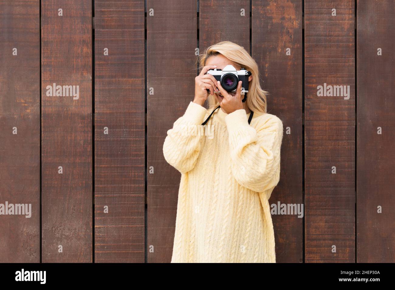 Donna che scatta una foto con una macchina fotografica mentre si appoggia su una parete di legno Foto Stock