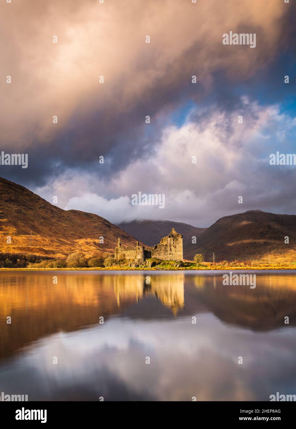 Kilchurn Castle, Loch awe, Argyll & Bute, Scozia. Caldi colori del tramonto che colpiscono le montagne e illuminano il castello, con spettacolari nuvole di tempesta nel cielo. Foto Stock