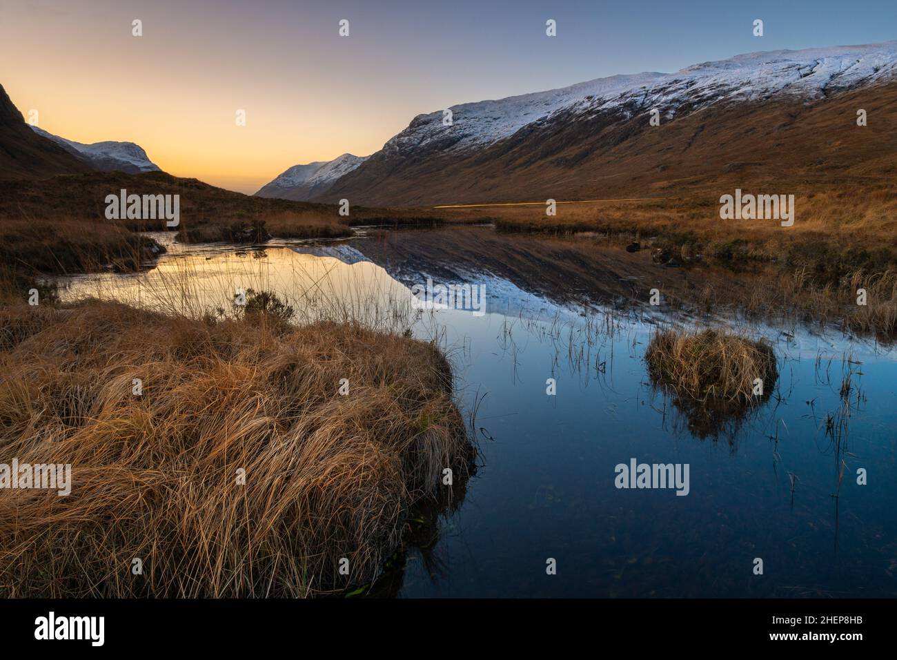 Glencoe Scotland, Lochan na Fola, in piedi in paludi altopiani e erba profonda, montagne innevate a sinistra e destra e uno specchio riflessione sull'acqua. Foto Stock