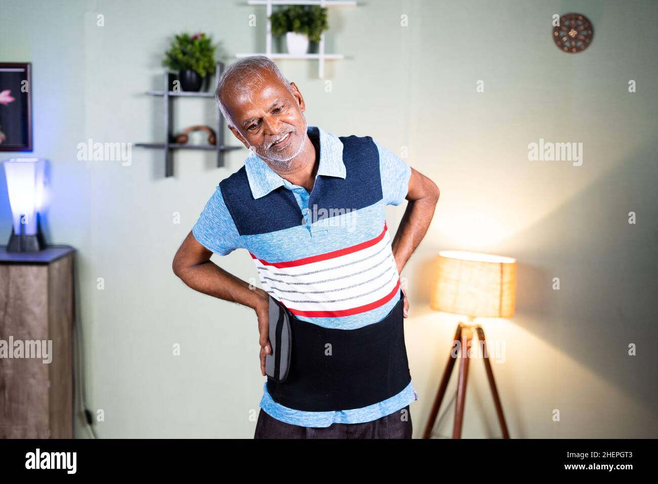 L'uomo anziano indiano felice ha ottenuto il rilievo dopo l'uso o l'uso della cinghia o del rinforzo di rilievo di dolore della schiena nel paese - concetto di rilassamento dall'uso della cinghia del supoort della schiena Foto Stock