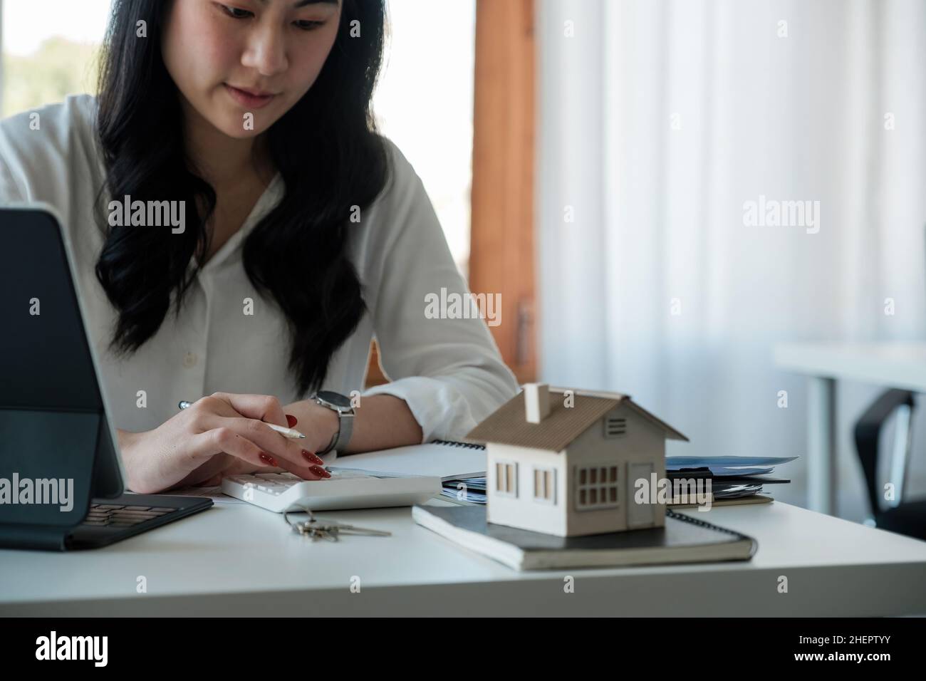 Comprando e vendendo le case ed i prezzi del bene immobile concetto. Donna usando la calcolatrice per contare l'affitto, i soldi o il costo di assicurazione della casa. Calcolo ipoteca Foto Stock
