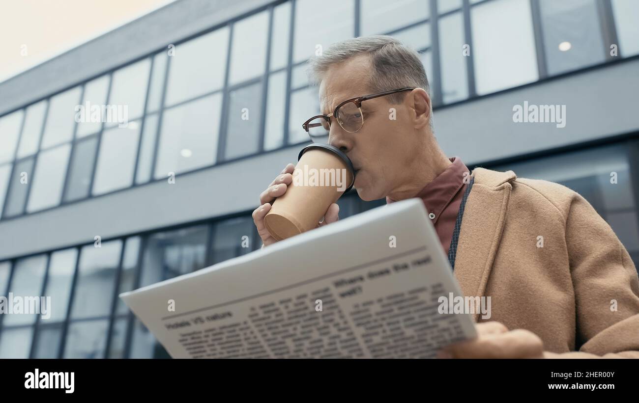 Uomo d'affari maturo bere caffè e leggere giornale all'aperto Foto Stock