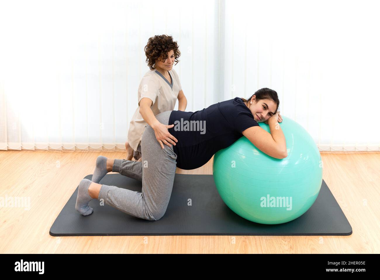 Una donna incinta che fa pilates gli esercizi con una sfera con l'aiuto del suo fisioterapista Foto Stock