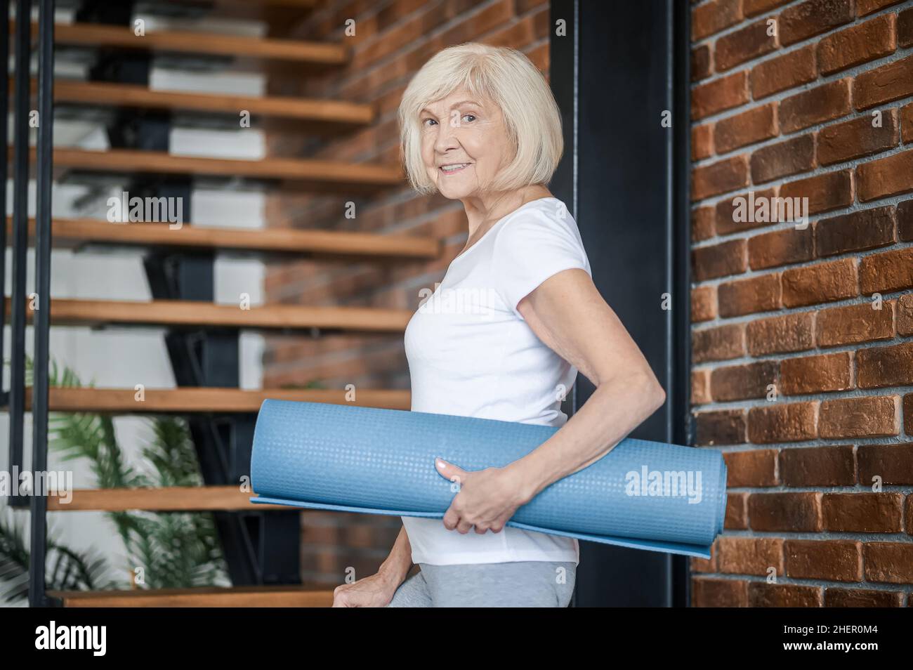 Donna anziana sottile con tappetino yoga in mano Foto Stock