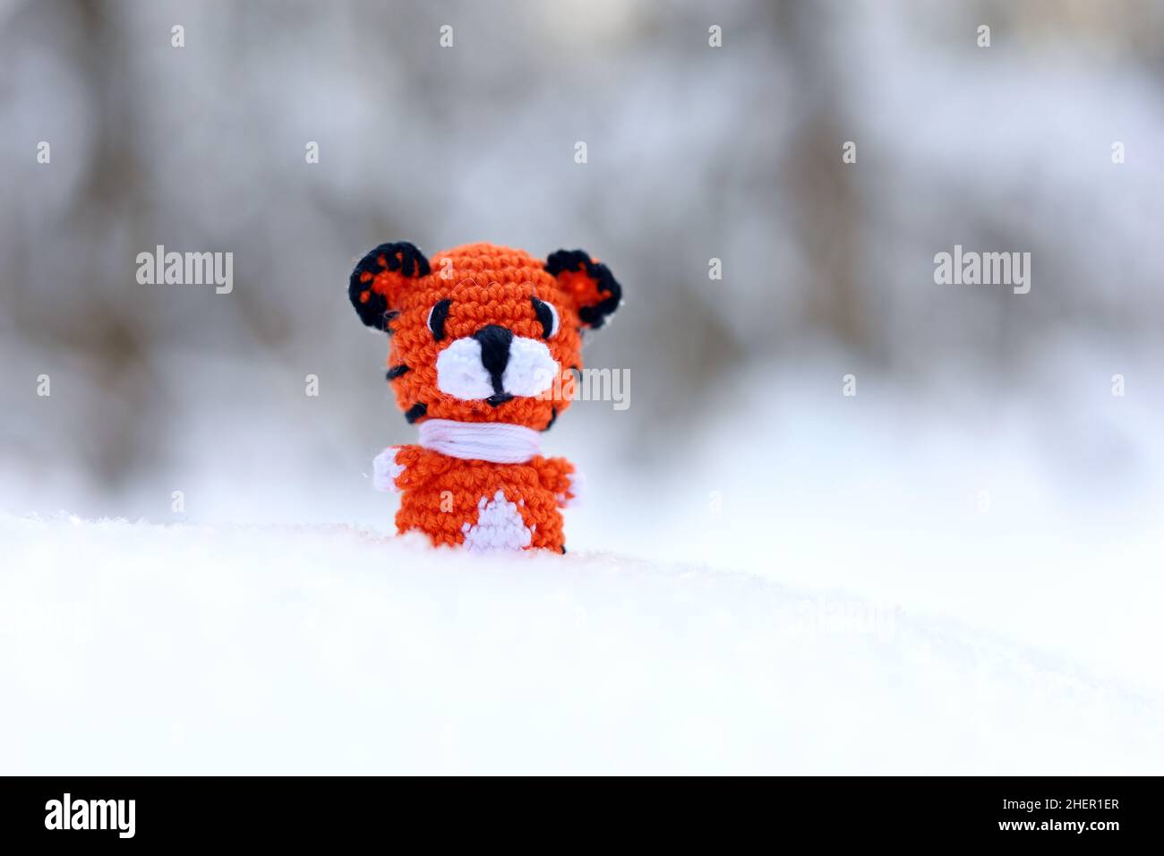 Tigre giocattolo lavorato a maglia sulla neve in una foresta. Sfondo per biglietto di auguri di festa Capodanno 2022 della tigre secondo il calendario cinese Foto Stock