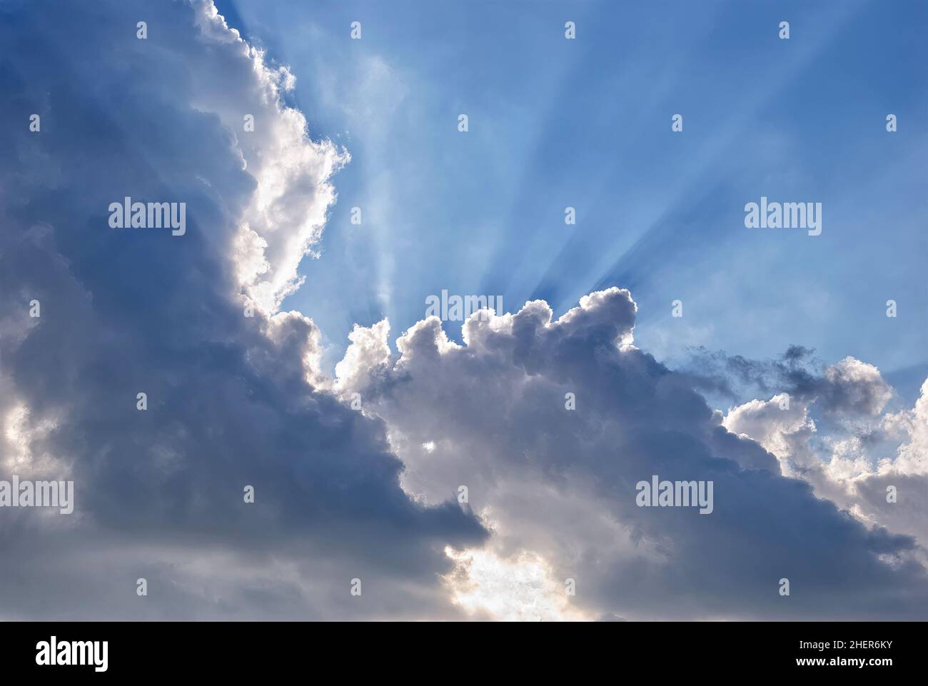 Raggi del sole che irradiano attraverso la parte superiore di alcune grandi nuvole di cumuli Foto Stock