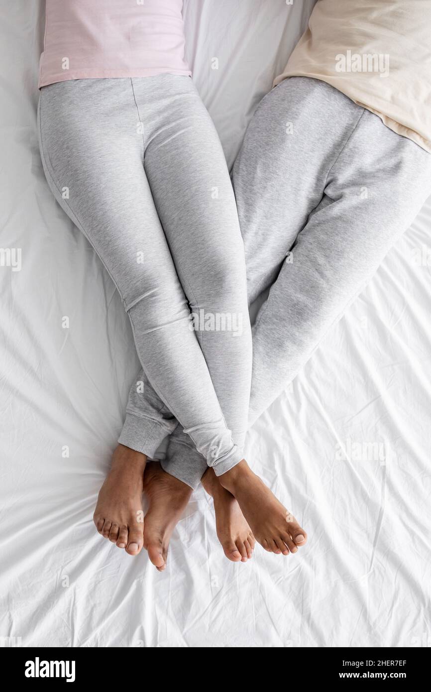 Donna annoamericana ritagliata millenaria in abiti domestici ha messo i piedi sull'uomo su letto bianco comfort Foto Stock