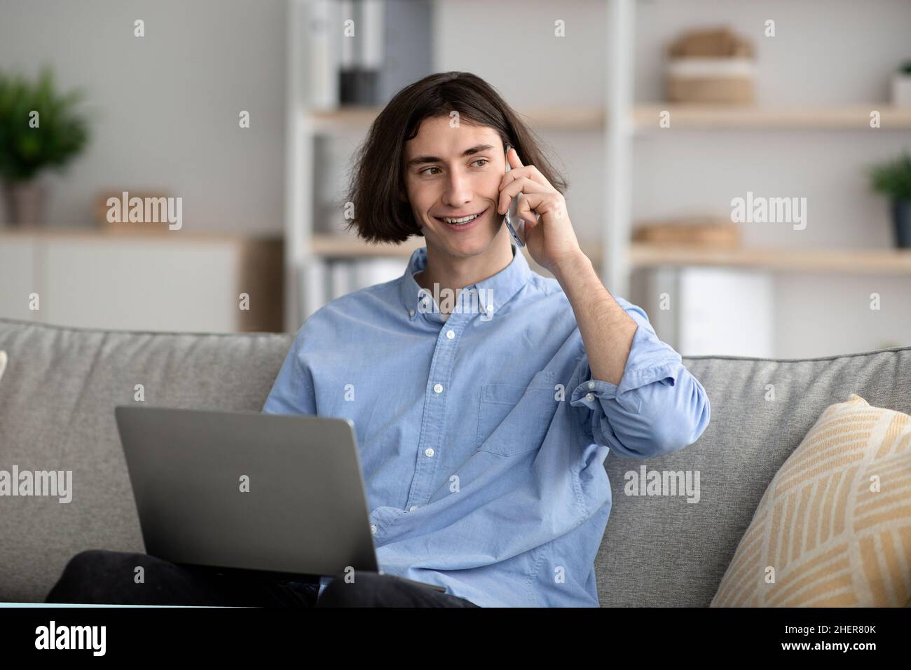 Giovane freelance che ha una conversazione telefonica mentre lavora su un notebook da casa, guardando da parte lo spazio per le copie Foto Stock