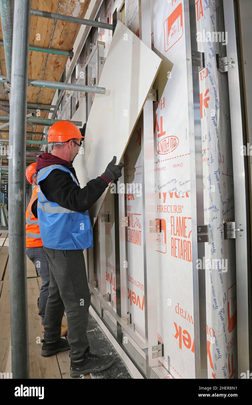 I lavoratori riparano pannelli di rivestimento ignifughi e un isolamento termico aggiuntivo alla parete esterna di un condominio londinese durante i lavori di ristrutturazione Foto Stock