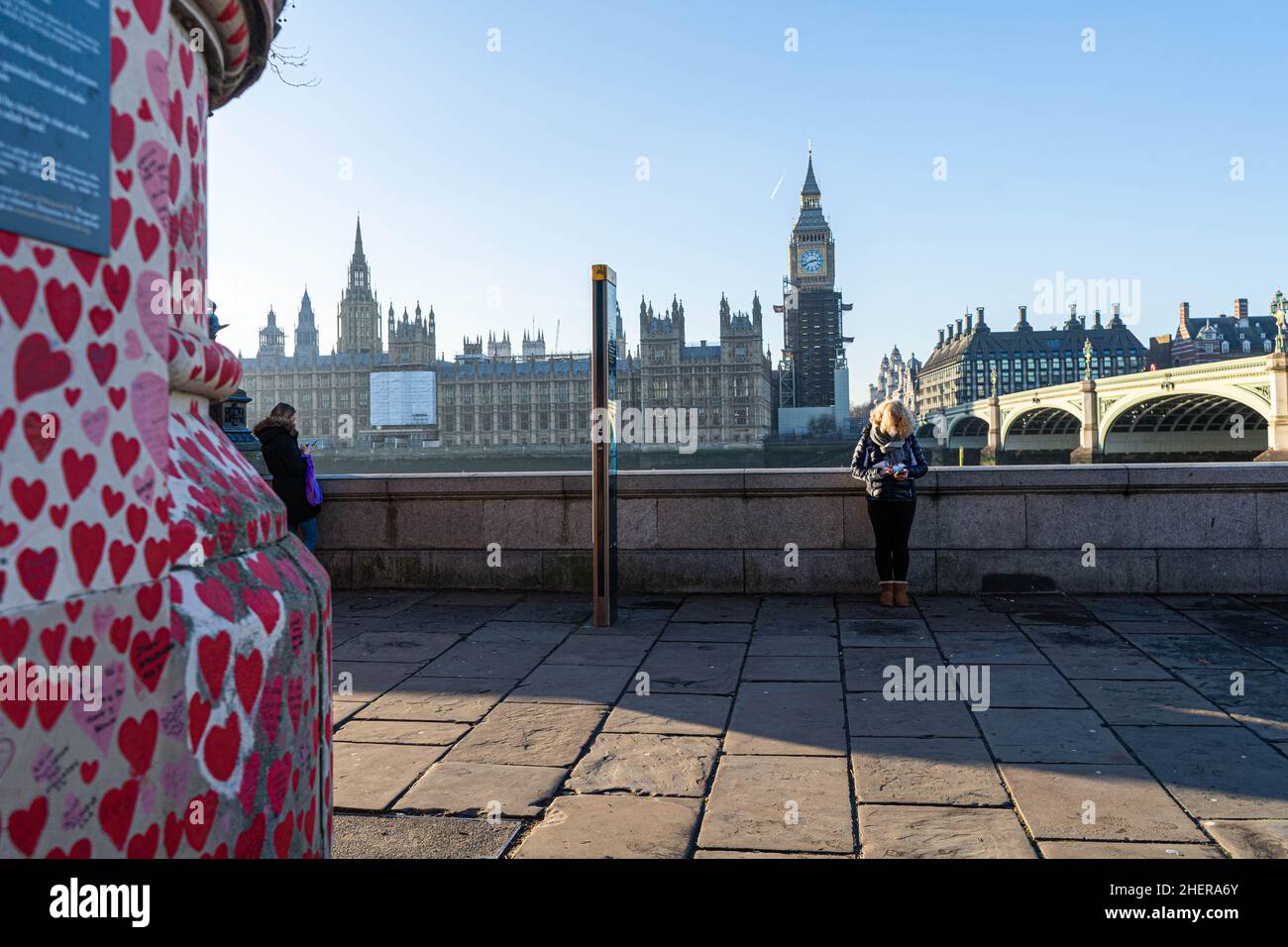 WESTMINSTER, LONDRA, REGNO UNITO. 12 gennaio 2022. La gente cammina al sole del pomeriggio lungo il National Covid Memorial Wall dipinto con cuori rossi sull'argine del Tamigi per commemorare le vittime della pandemia del COVID-19 il giorno in cui il primo ministro Boris Johnson ha affrontato l'esame in Parlamento dopo aver ammesso di aver partecipato a una festa in giardino a Downing Street il 20 Maggio 2020, in un momento in cui il Regno Unito era soggetto a restrizioni per il coronavirus. Credit: amer Ghazzal/Alamy Live News Foto Stock