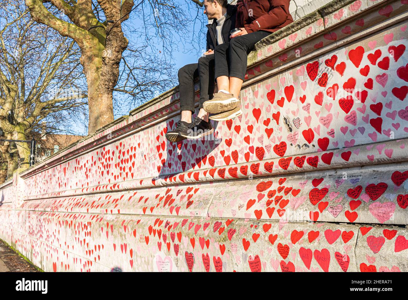 WESTMINSTER, LONDRA, REGNO UNITO. 12 gennaio 2022.Una coppia seduta al sole del pomeriggio sulla cima del National Covid Memorial Wall dipinta con cuori rossi sull'argine del Tamigi per commemorare le vittime della pandemia del COVID-19 il giorno in cui il primo ministro Boris Johnson scrutinio affrontato in Parlamento dopo aver ammesso di aver partecipato ad una festa in giardino A Downing Street il 20 maggio 2020, in un momento in cui il Regno Unito era soggetto a restrizioni per il coronavirus. Credit: amer Ghazzal/Alamy Live News Foto Stock