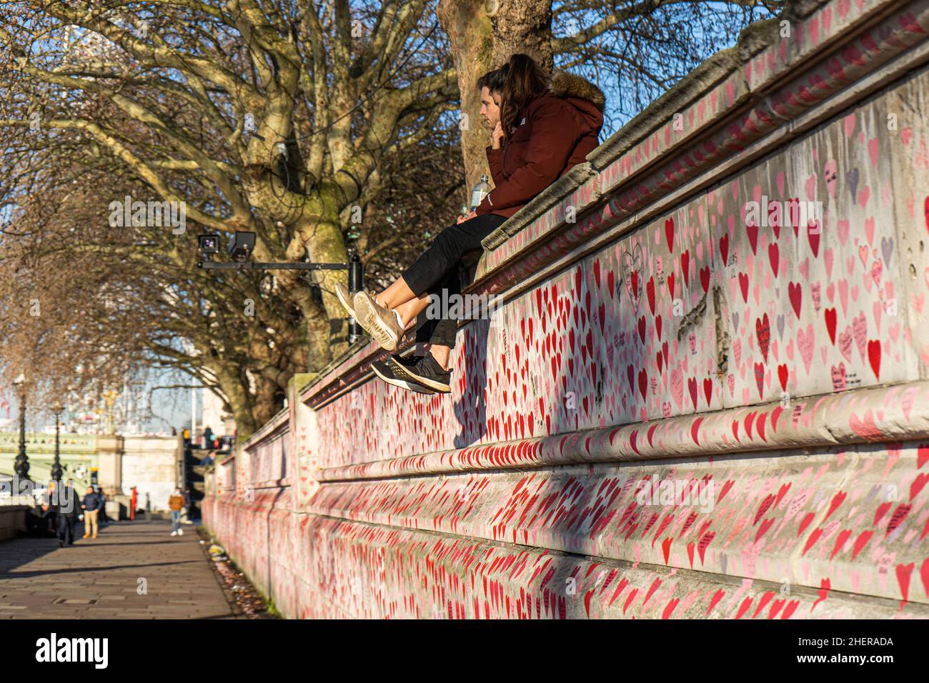 WESTMINSTER, LONDRA, REGNO UNITO. 12 gennaio 2022.Una coppia seduta al sole del pomeriggio sulla cima del National Covid Memorial Wall dipinta con cuori rossi sull'argine del Tamigi per commemorare le vittime della pandemia del COVID-19 il giorno in cui il primo ministro Boris Johnson scrutinio affrontato in Parlamento dopo aver ammesso di aver partecipato ad una festa in giardino A Downing Street il 20 maggio 2020, in un momento in cui il Regno Unito era soggetto a restrizioni per il coronavirus. Credit: amer Ghazzal/Alamy Live News Foto Stock