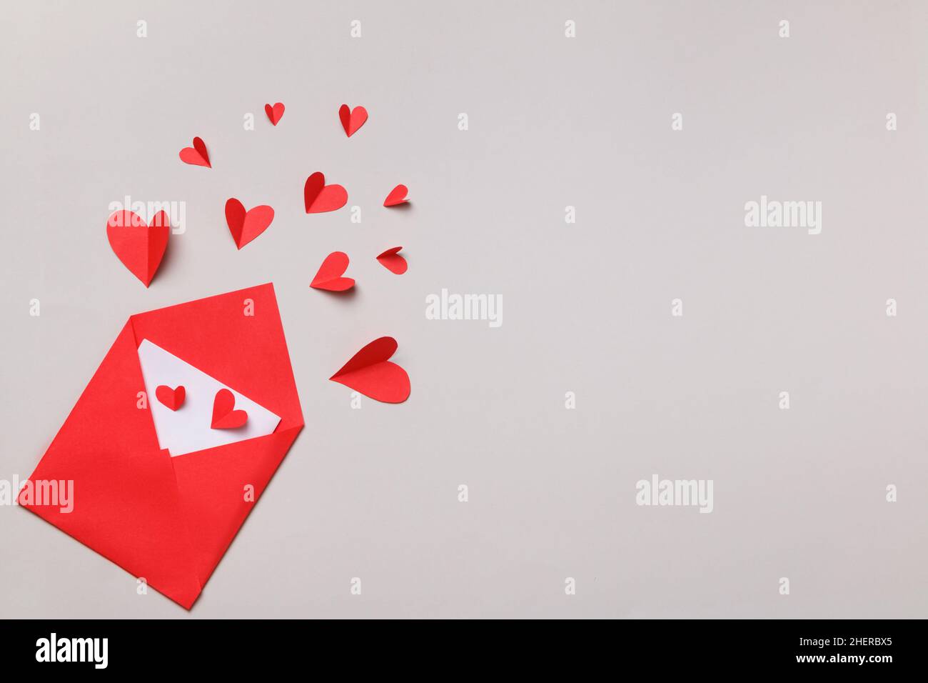 Busta di carta rossa con una nota bianca all'interno e cuori su sfondo grigio pastello. Lettera d'amore per San Valentino. Disposizione piatta, vista dall'alto. Foto Stock