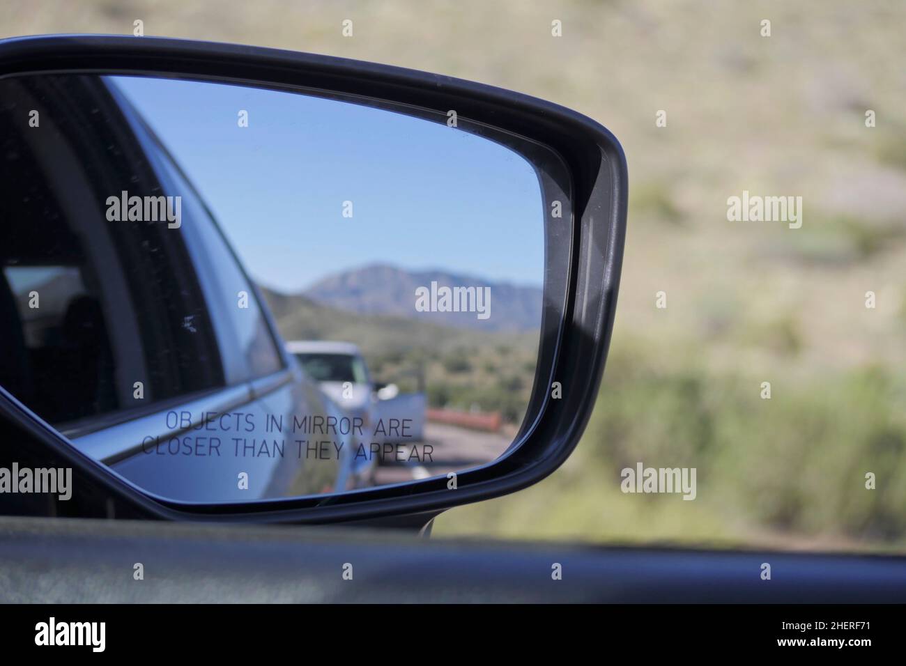 Guardando il traffico, su un'autostrada montagnosa dell'Arizona settentrionale, attraverso lo specchio con vista laterale con auto e montagne sullo sfondo. Foto Stock