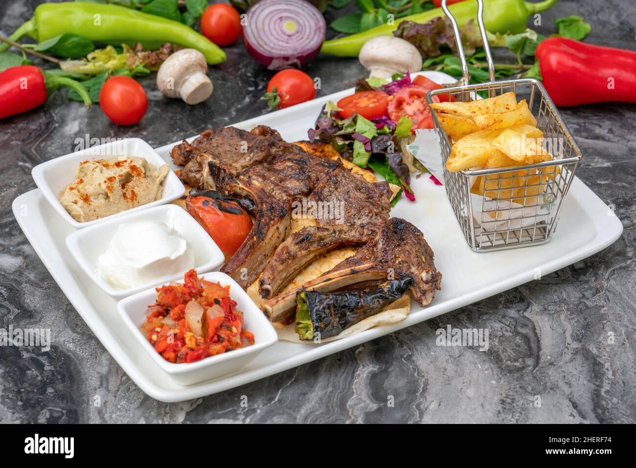 Costolette di agnello alla griglia con patatine fritte e antipasti su un piatto di porcellana bianca Foto Stock