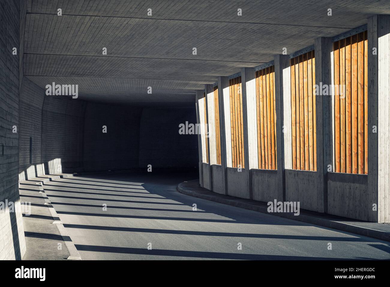 La galleria delle valanghe con doghe in legno si estende in un tunnel di strada in cemento scuro Foto Stock