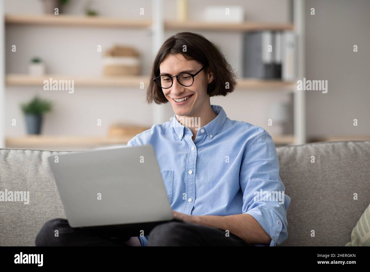 Lavoro a distanza. Ragazzo libero felice che lavora con il laptop a casa, seduto sul divano, godendo di opportunità di lavoro a distanza Foto Stock