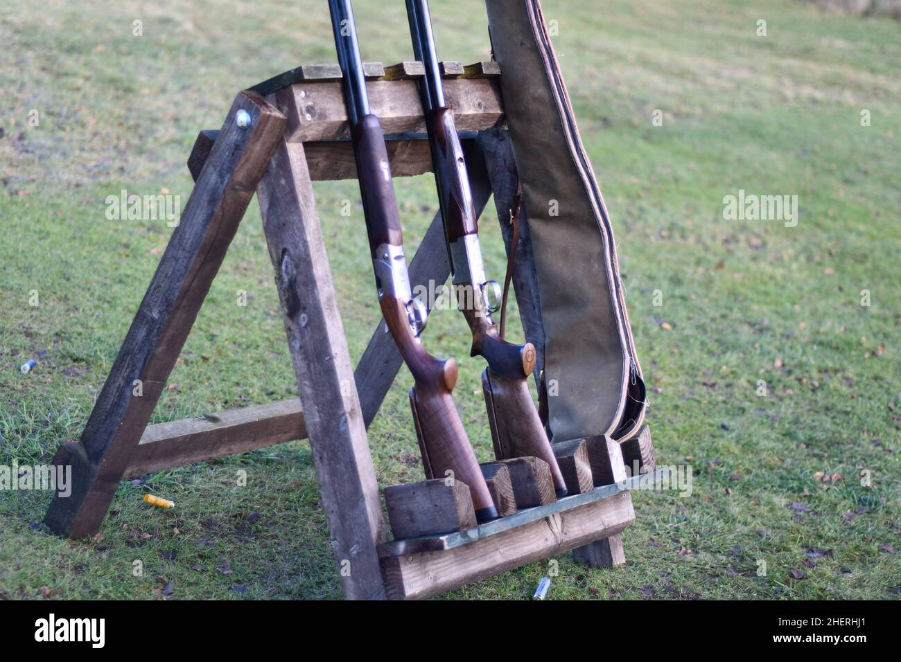 Cavalletto esterno in legno che tiene due fucili e una cassa con cartucce usate sul prato Foto Stock