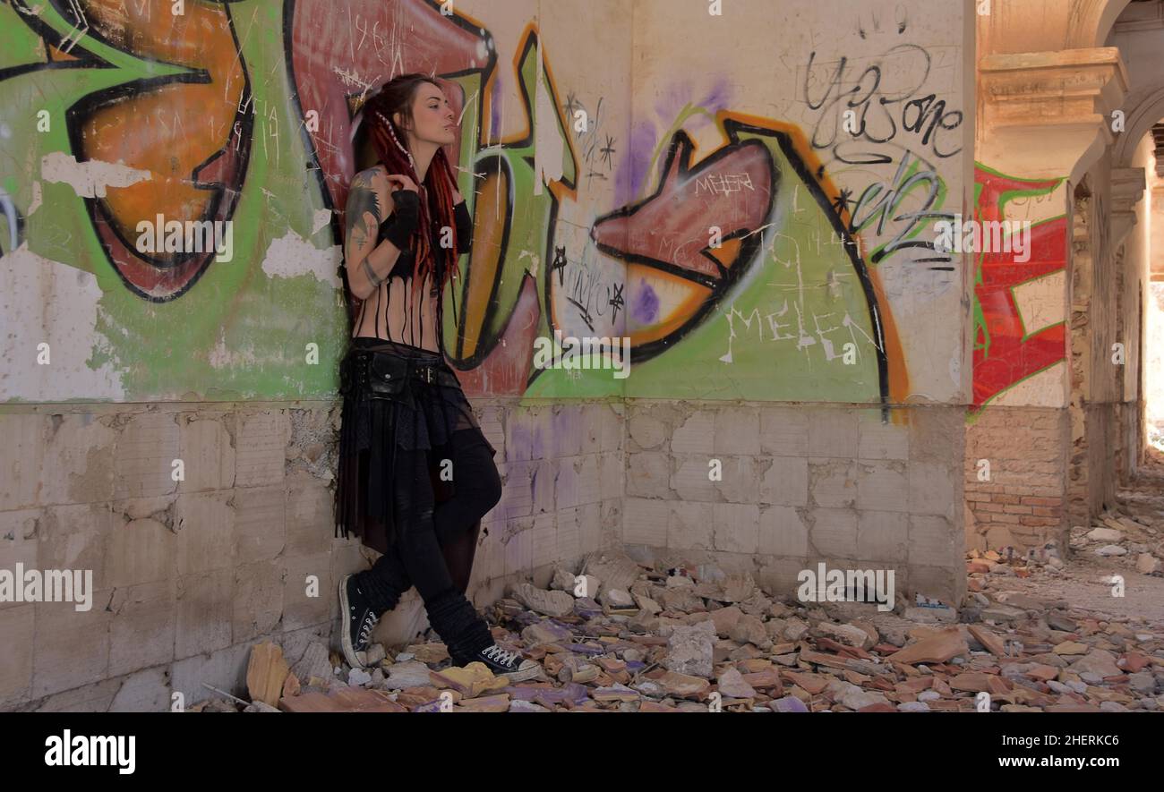 Giovane donna con tatuaggi e lucchetti si erge contro il muro con graffiti di una casa abbandonata Foto Stock