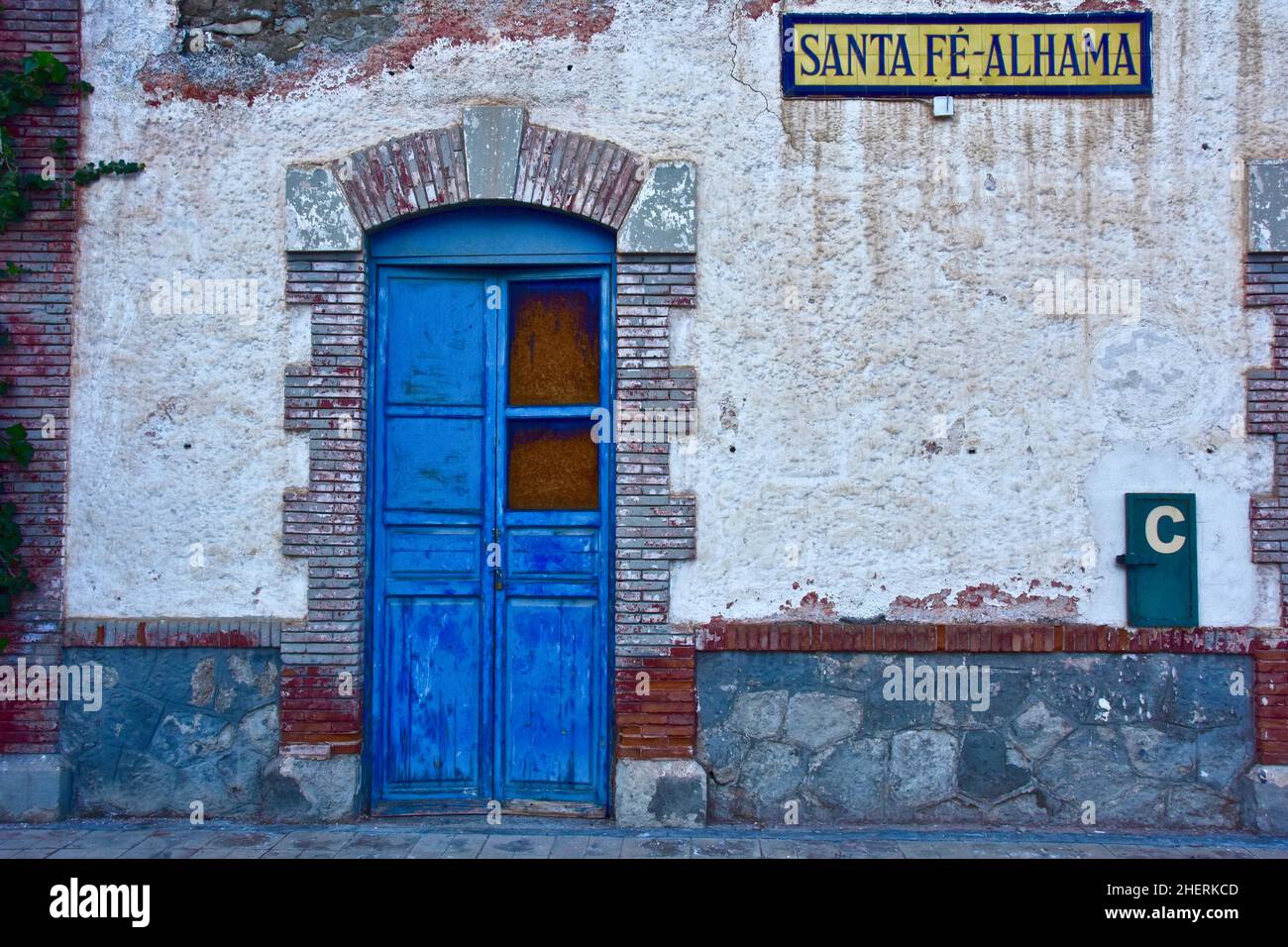 Porta a chiodata blu incorniciata da mattoni a stazione chiusa, Santa Fe-Alhama, Andalusia, Spagna Foto Stock