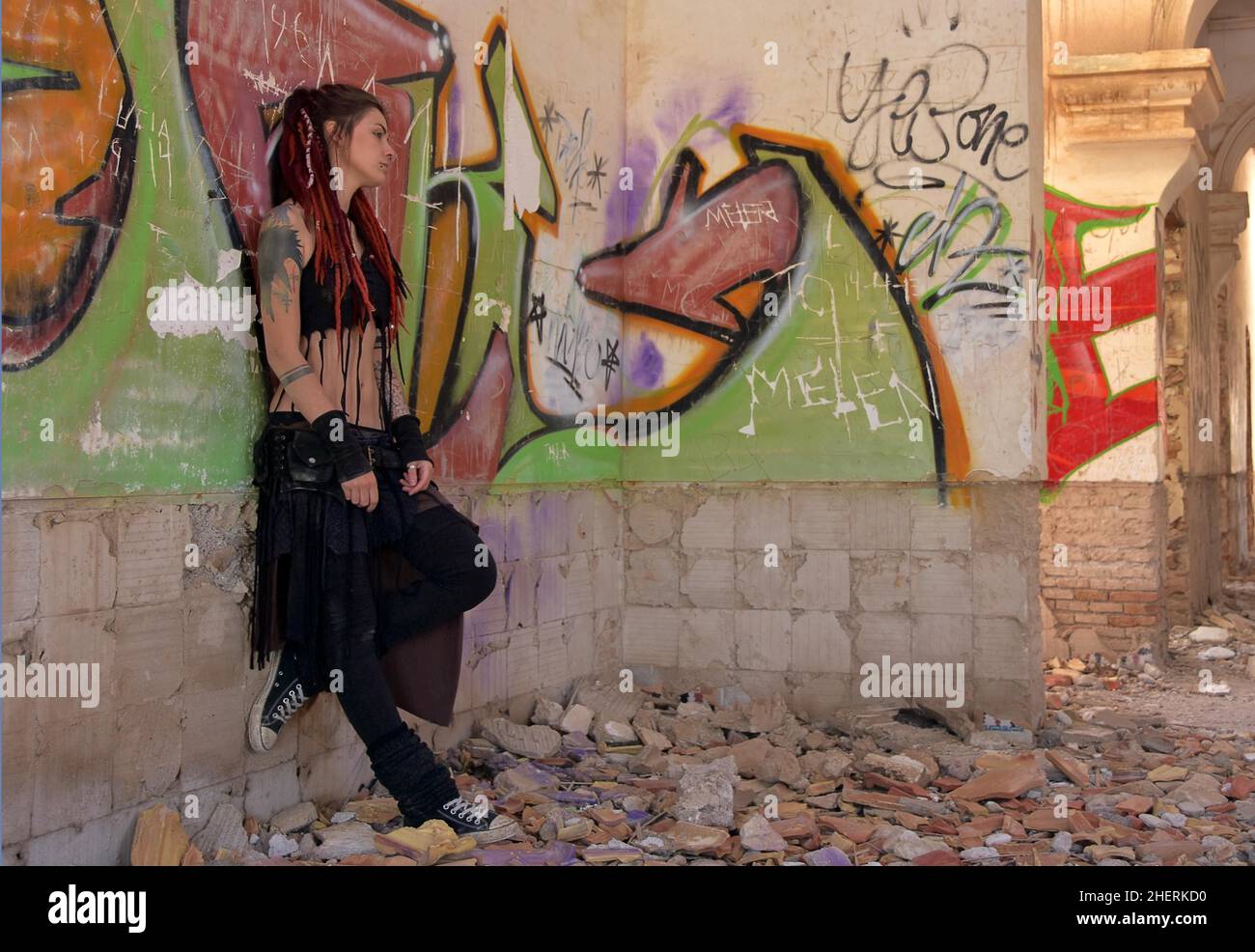 Giovane donna con tatuaggi e lucchetti si erge contro il muro con graffiti di una casa abbandonata Foto Stock