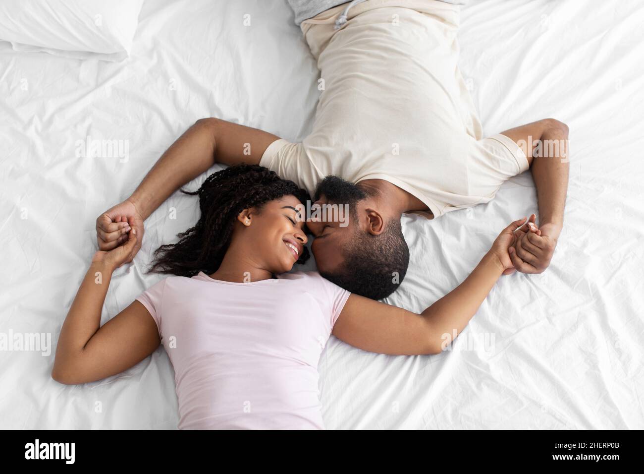 Sorridente giovane afroamericana signora e ragazzo godere di momento romantico sdraiati su un comodo letto in camera da letto, vista dall'alto Foto Stock