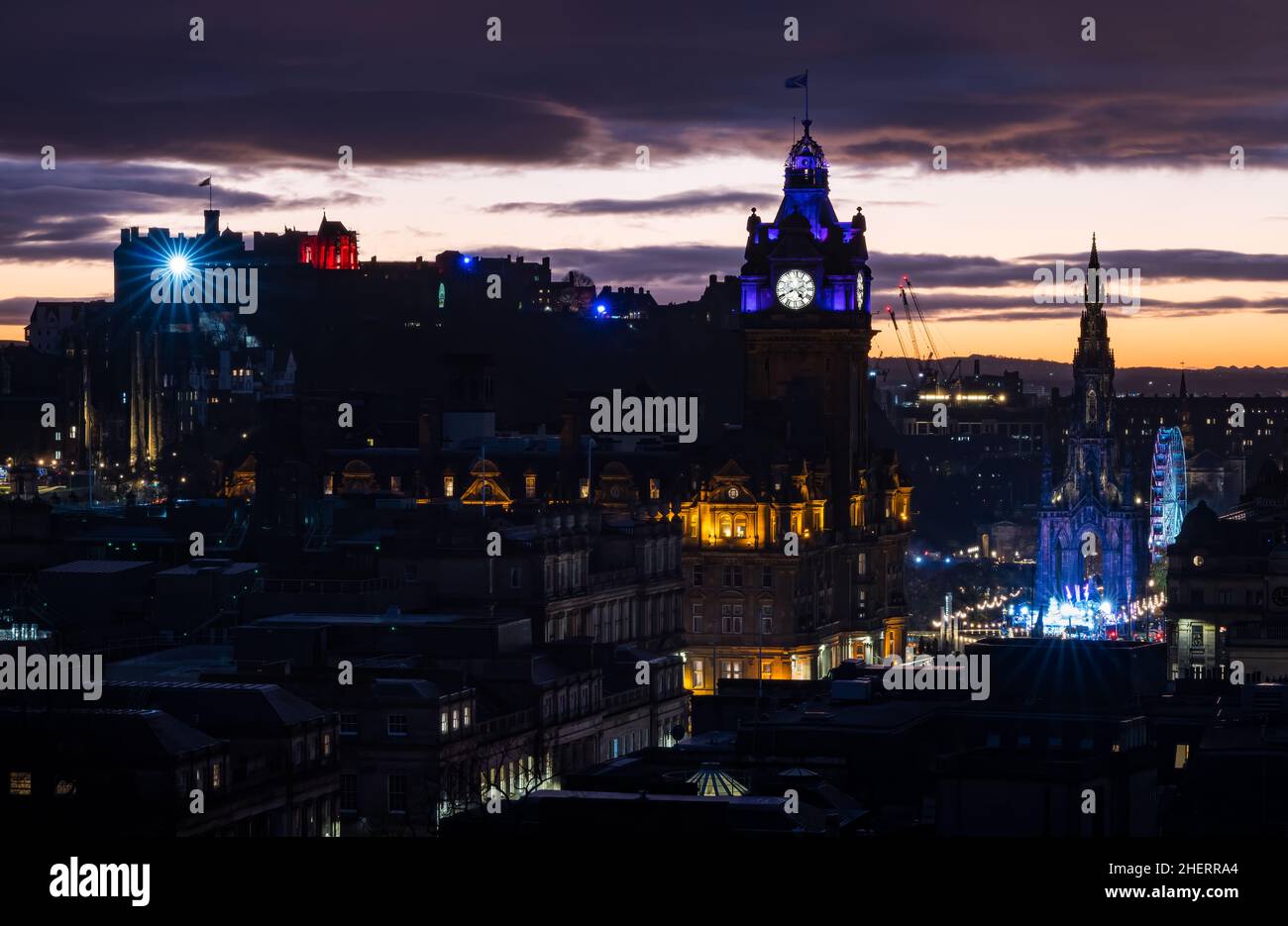 Uno spettacolo di luci dal Castello di Edimburgo visto sullo skyline della città con un tramonto arancione colorato e luci natalizie, Edimburgo, Scozia, Regno Unito Foto Stock