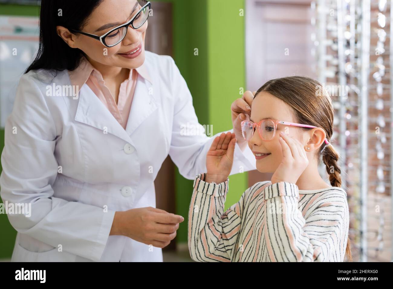sorridente oculista asiatico scegliendo occhiali per ragazza in negozio di ottica Foto Stock