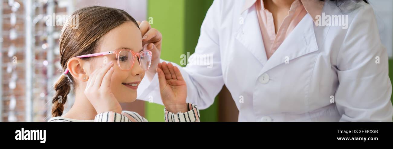 ragazza positiva scelta occhiali vicino oftalmologo in ottica salone, banner Foto Stock