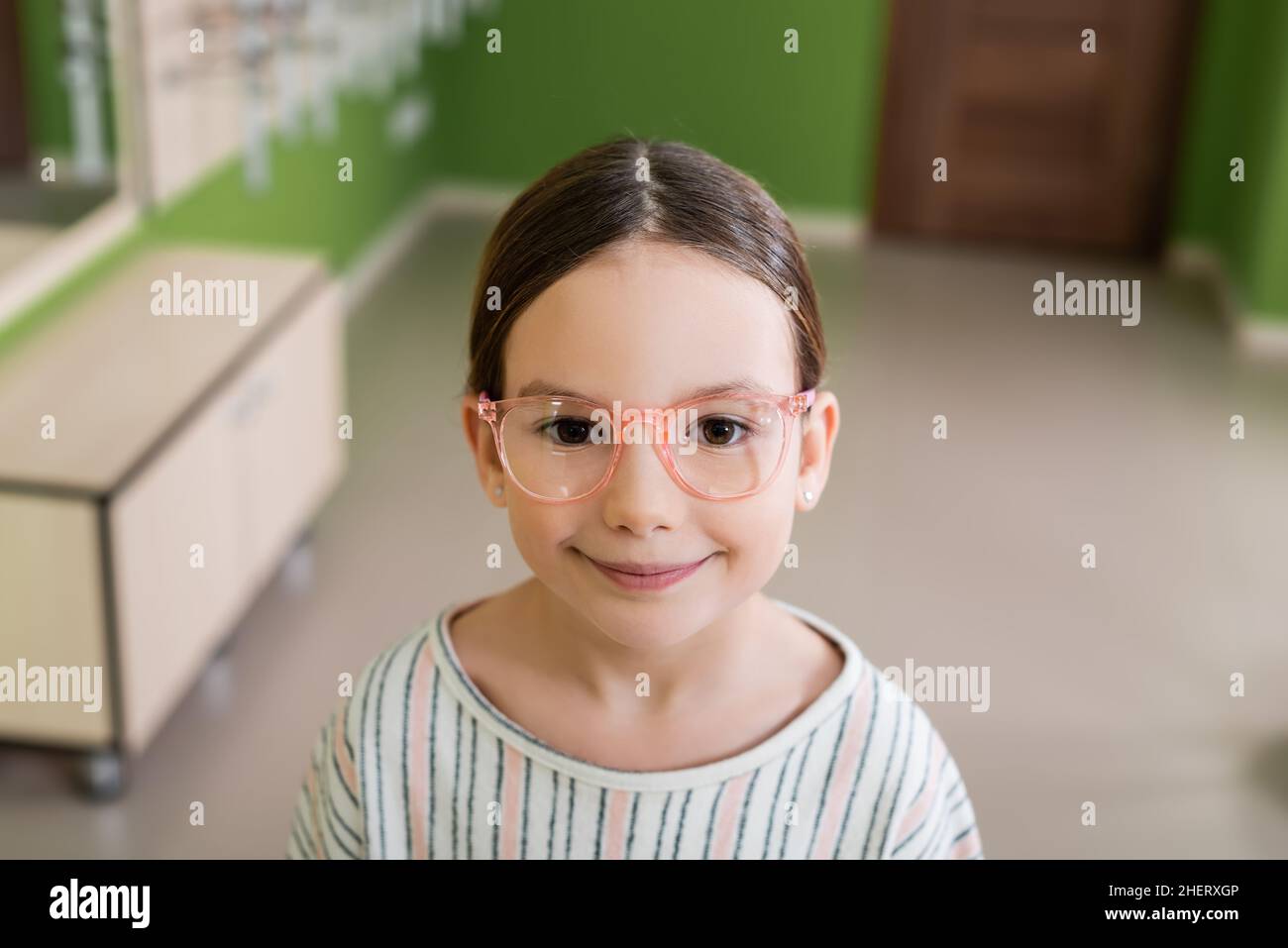 ragazza felice in occhiali guardando la macchina fotografica in negozio ottica su sfondo sfocato Foto Stock