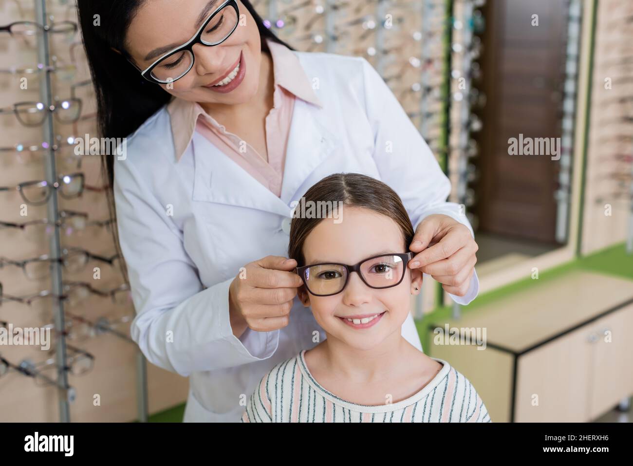 sorridente oculista asiatico scelta occhiali per ragazza felice guardando la macchina fotografica in negozio di ottica Foto Stock