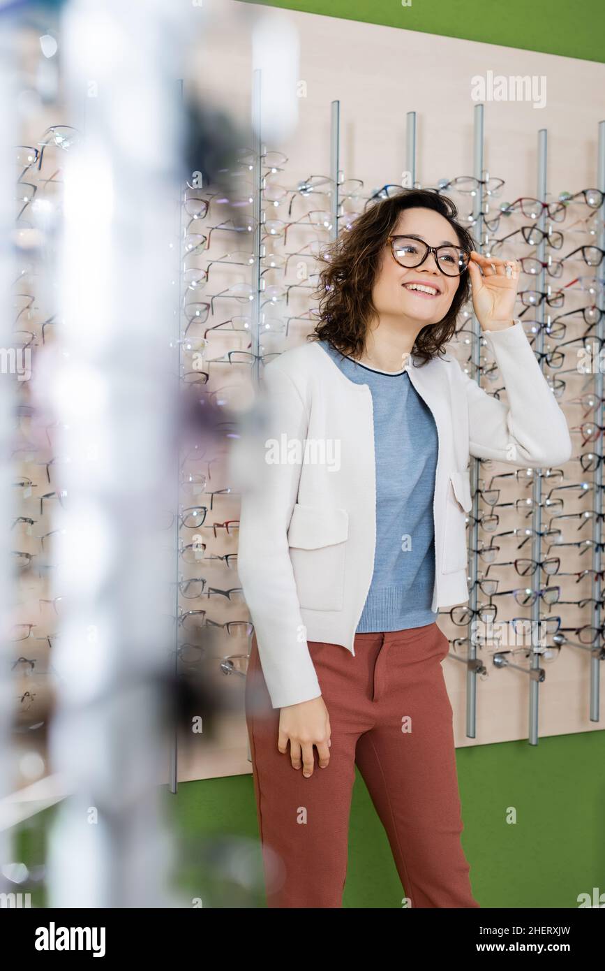 donna felice che prova sugli occhiali in ottica negozio in primo piano sfocato Foto Stock